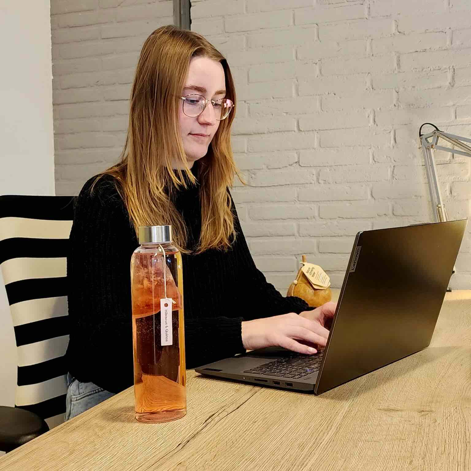 Oprichter van oostaMo werkt op een laptop aan internationale orders met een fles koud gezette Overnight Botanicals op haar bureau